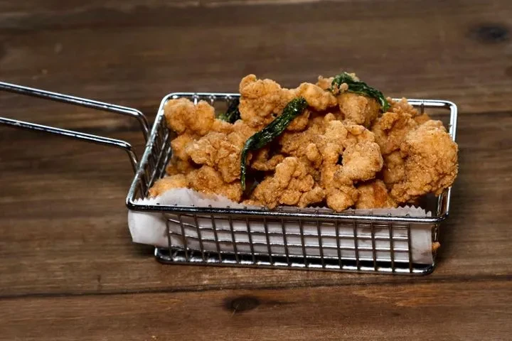 Golden-brown fried chicken pieces and basil in a metal basket on wood.