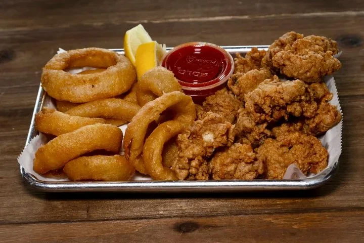 Metal tray of fried onion rings, chicken, sauce, and lemon.