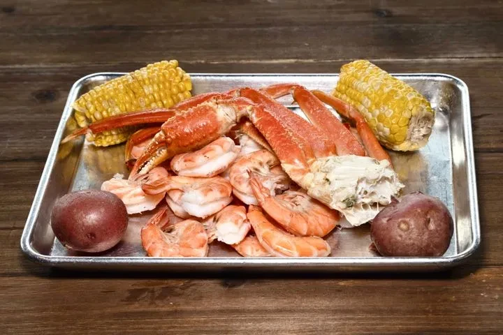 Seafood boil with crab, shrimp, corn, and potatoes on a tray.