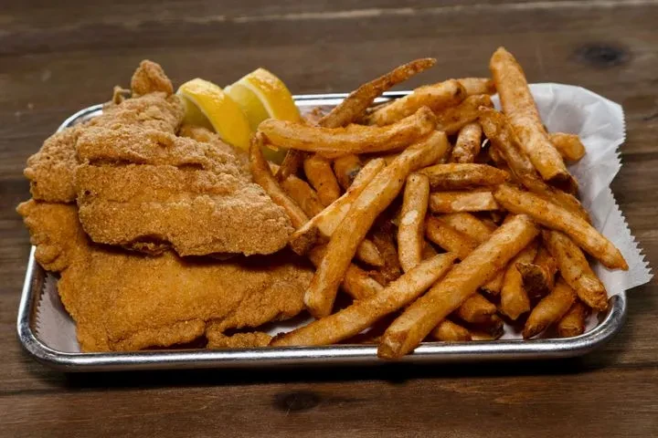 Fried fish, french fries, and lemon wedges on a silver tray.