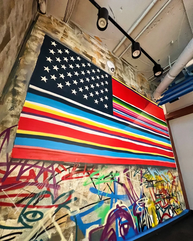 Colorful flag-inspired mural and graffiti on a textured industrial wall.
