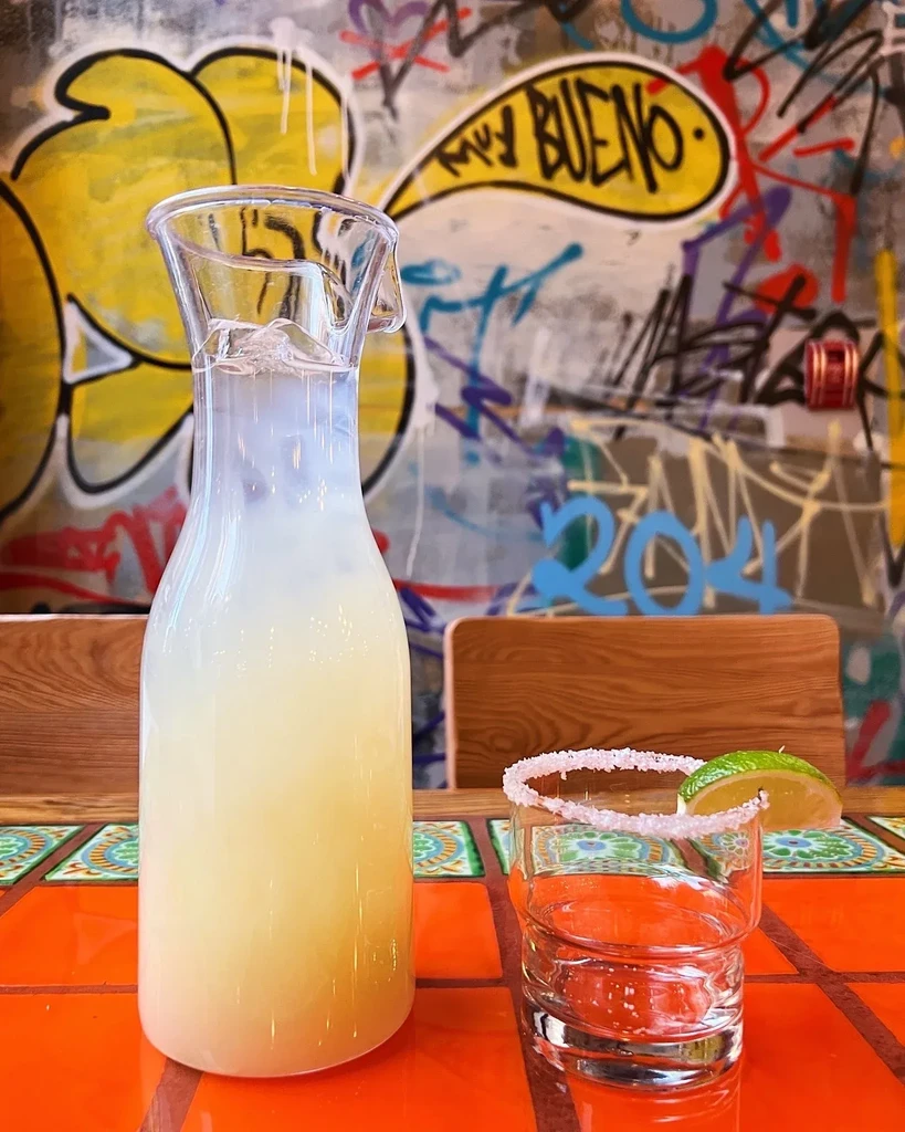 Pitcher and glass on orange tiled table, colorful graffiti background.