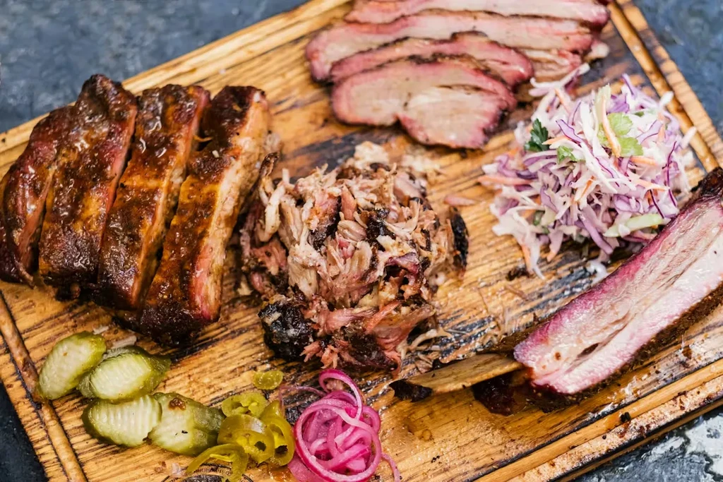 Assorted barbecue meats and pickled sides on a rustic wooden board.