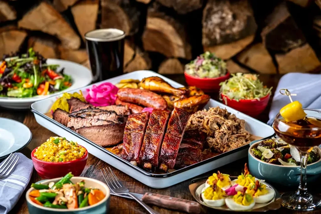 Lavish barbecue meats, diverse sides, and drinks on rustic wooden table.