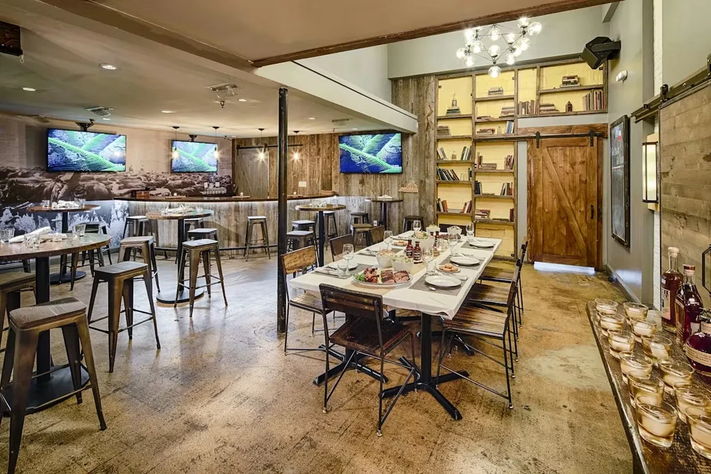 Rustic-industrial restaurant interior with dining tables, bar, and cattle mural.