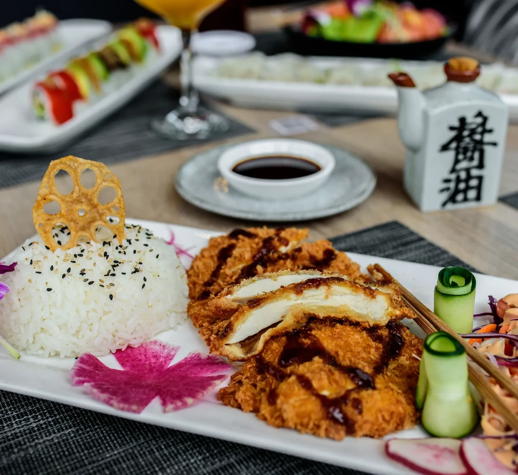 Plated Japanese fried chicken cutlet, rice, lotus root chip, and vegetables.