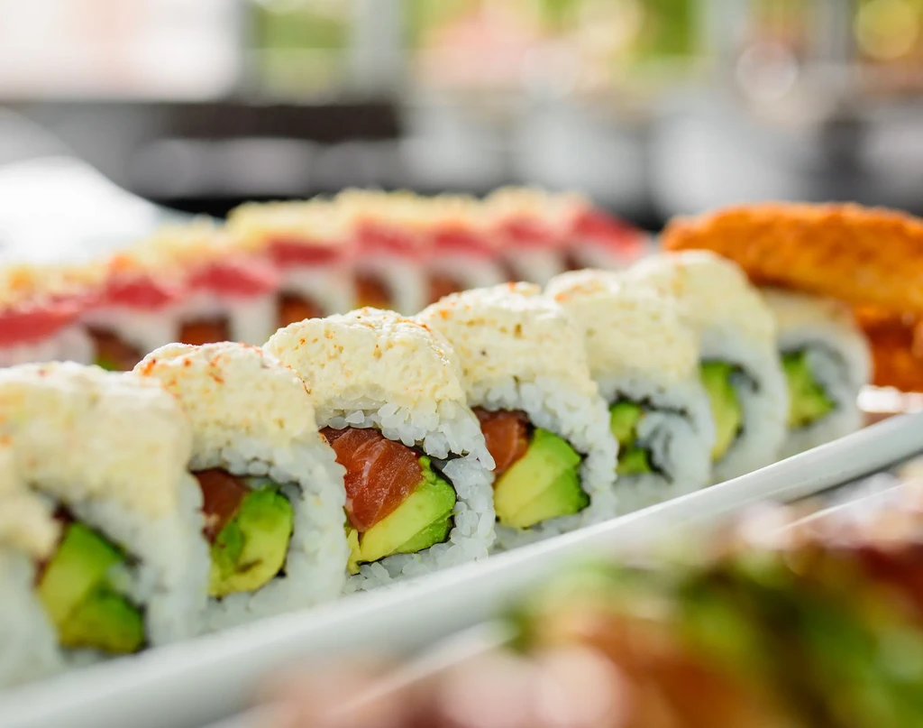 Rows of salmon and avocado maki sushi with a creamy topping.