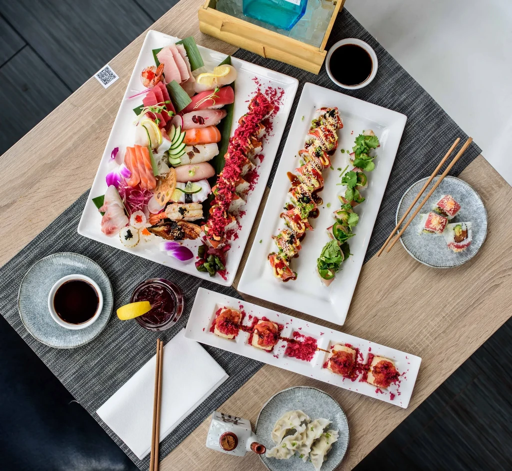 Overhead, artfully arranged Japanese sushi, sashimi, and gyoza meal on wood.