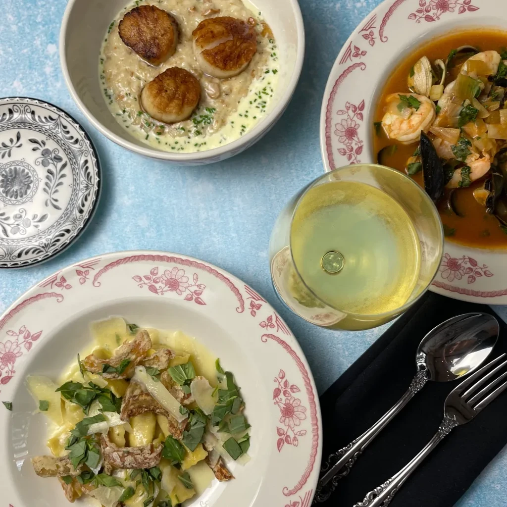 Flat lay of scallops, seafood stew, pasta, and white wine.