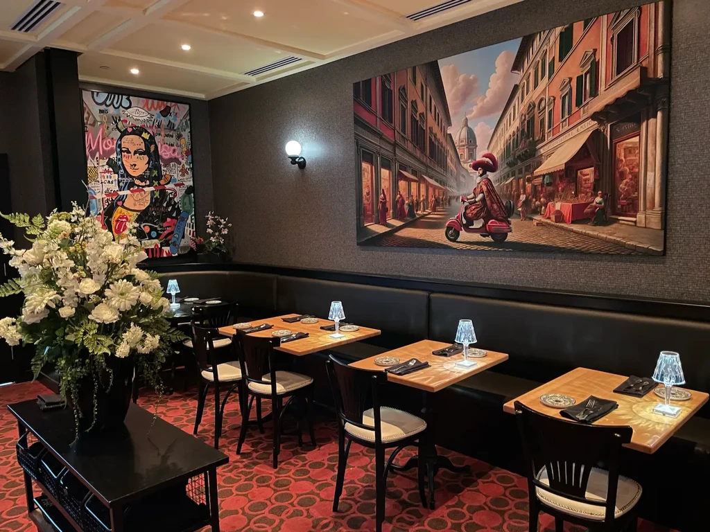 Empty restaurant interior with dark booths, red carpet, and large paintings.