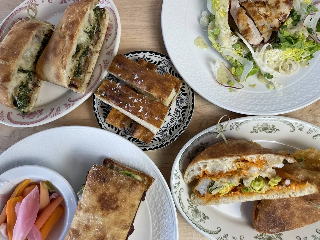 Overhead view of various sandwiches, chicken salad, focaccia, and pickled vegetables.