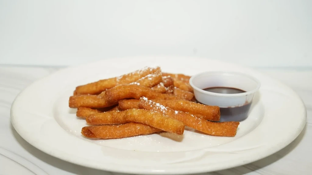 Fried churros dusted with powdered sugar and chocolate dipping sauce.