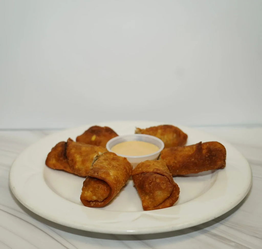 Six golden-brown crispy rolls on a plate with dipping sauce.