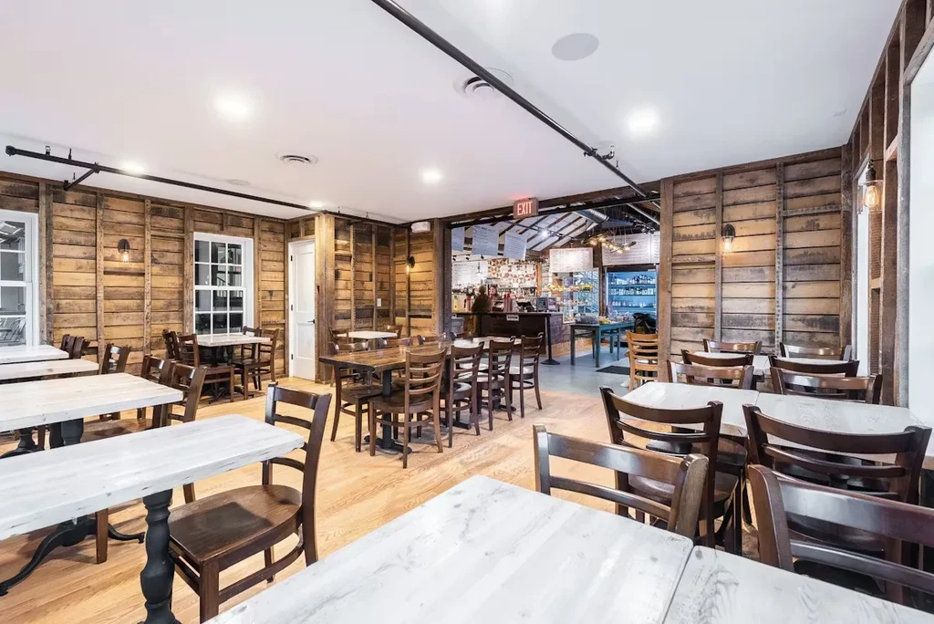 Rustic-industrial dining area with wooden walls, tables, and exposed pipes.