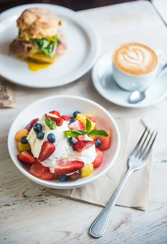 Vibrant fruit salad, latte, and breakfast sandwich on a wooden table.