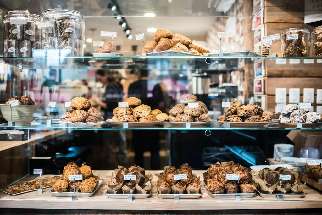 Croissants, scones, cookies, and muffins displayed with labels in a bakery case.