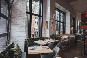 Empty modern restaurant with white brick, green velvet seating, and windows.