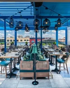 Modern rooftop restaurant interior: green booths, blue slatted roof, city view.