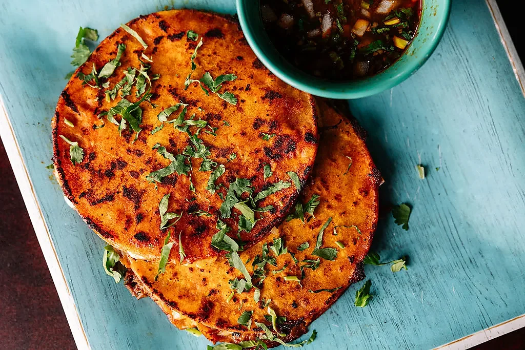 Two griddled quesadillas with cilantro beside a bowl of consomme
