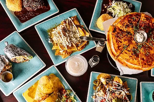 Overhead spread of Mexican dishes on teal plates with salsas