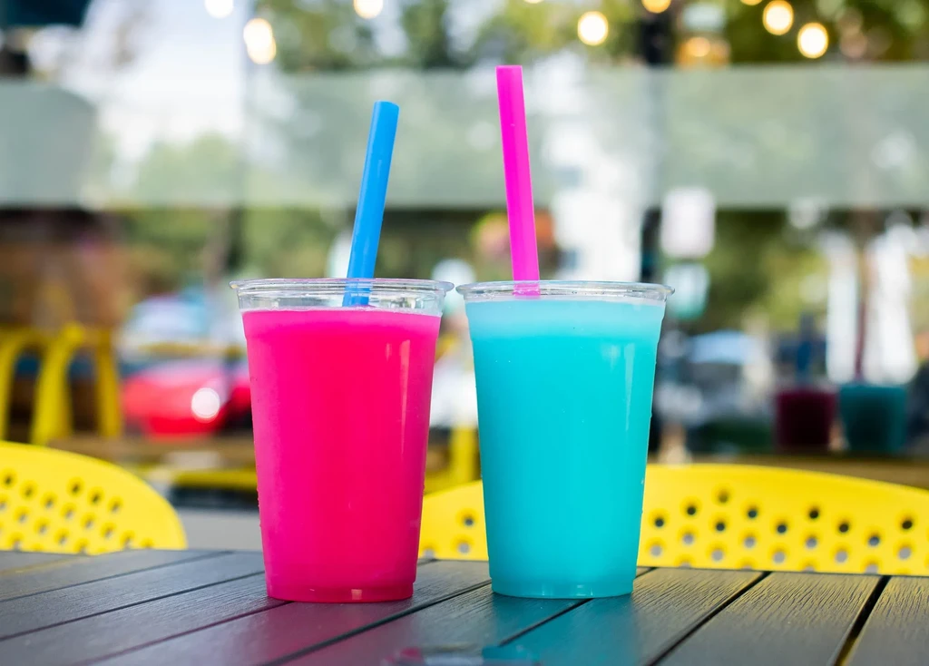 Two pink and blue slushies with straws on a table outdoors.
