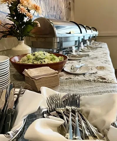 Buffet line with salad, hot food chafing dishes, plates, and cutlery.