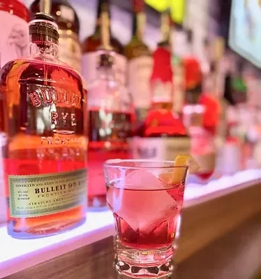 Bulleit Rye whiskey bottle, pink cocktail with ice and lemon peel.