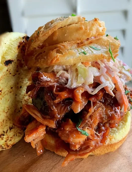 Pulled pork sandwich, coleslaw, onion rings, on a wooden board.