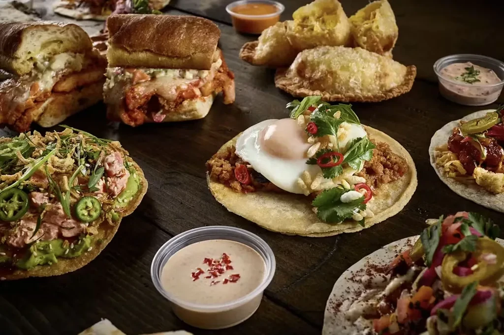 Spread of sandwiches, tostadas, tacos, and pastries on a rustic table.