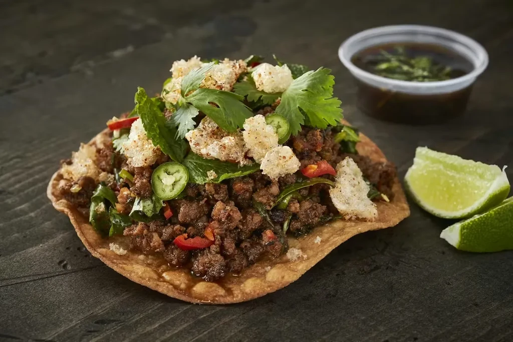 Crispy tortilla piled with seasoned meat, crunchy rinds, jalapeños, and lime.