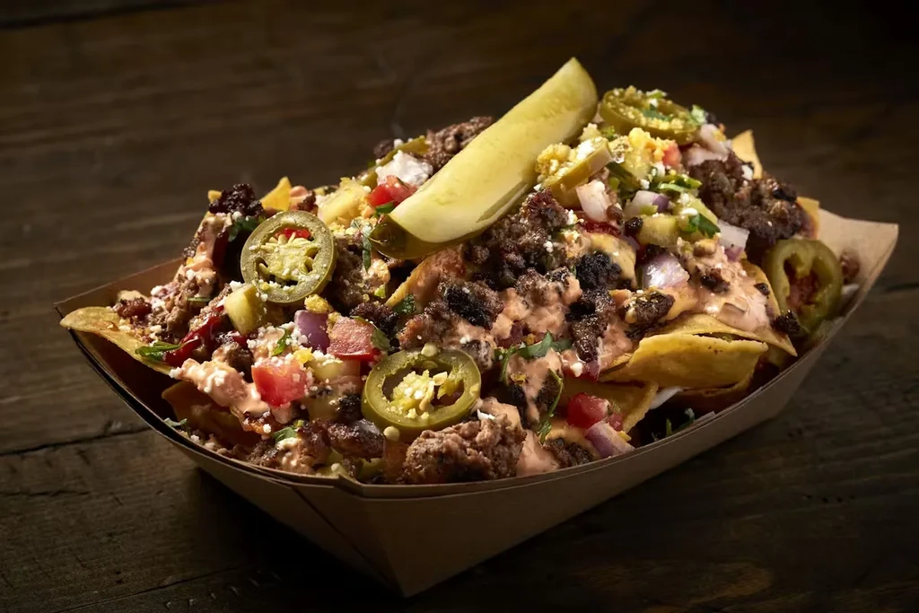 Loaded nachos with meat, cheese, jalapeños, and a pickle spear.