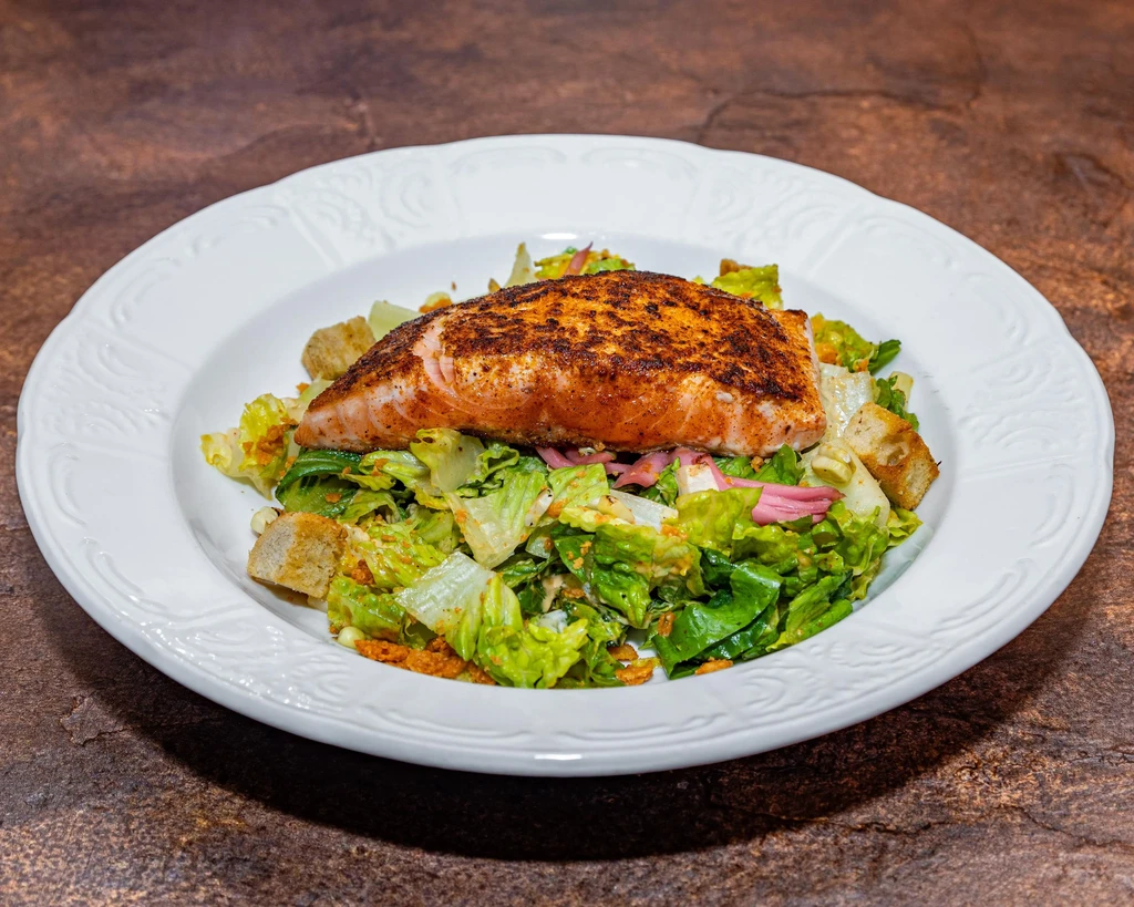 Plated salmon fillet with spices on green salad and croutons.