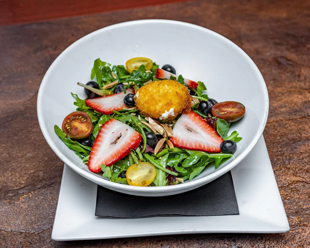 Colorful salad with fried cheese, berries, tomatoes, and almonds.