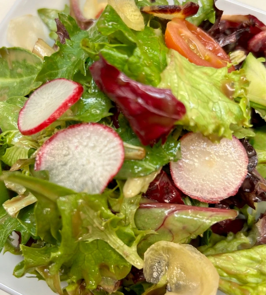 Vibrant mixed green salad with lettuce, red radishes, and tomato slices.