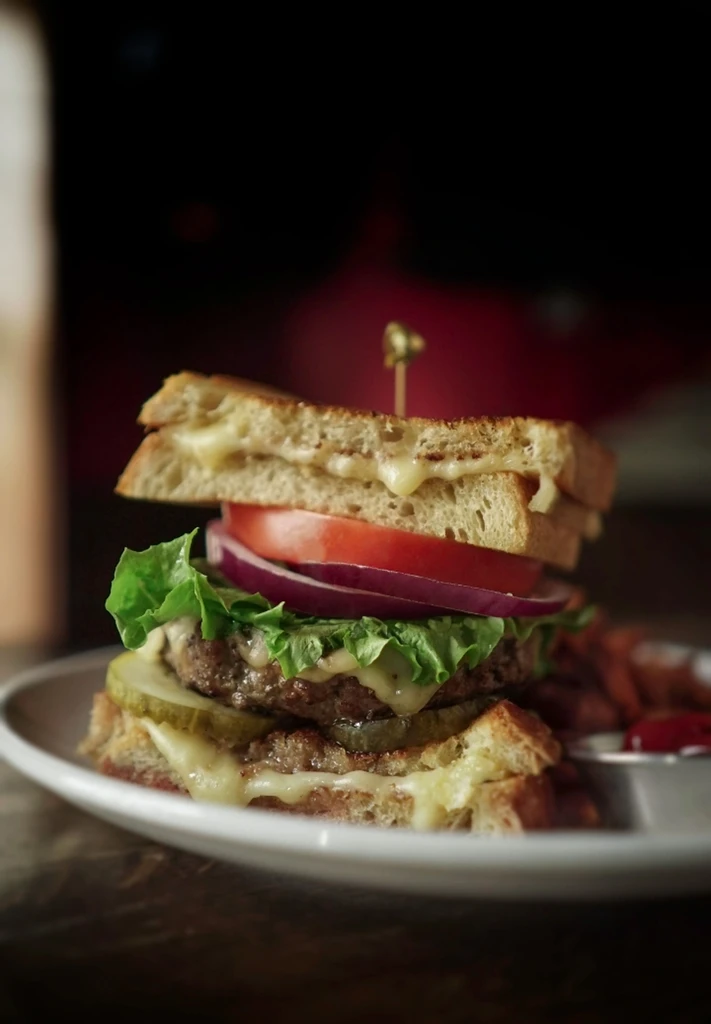 Towering burger with grilled cheese buns, beef patties, and vegetables.
