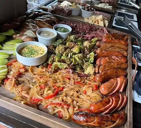 Large rustic wooden tray piled with sausages, Brussels sprouts, pretzels, and dips.
