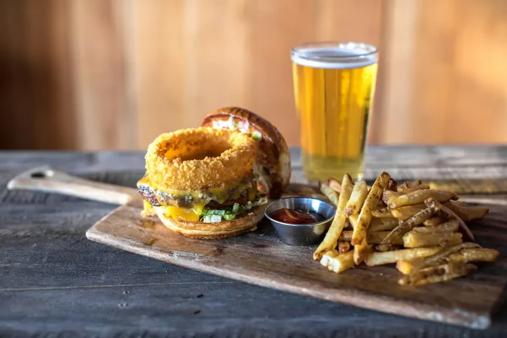 A burger, french fries, ketchup, and beer on a wooden board.