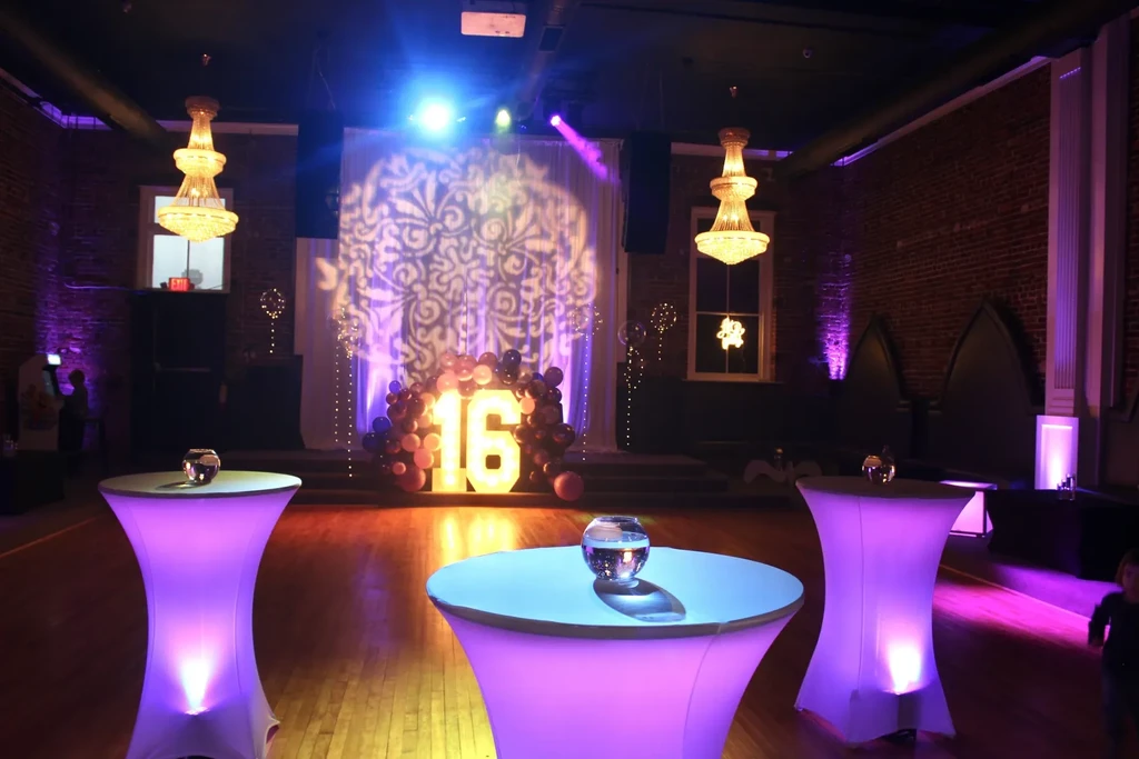 Lit party venue with glowing '16' sign, balloons, and cocktail tables.