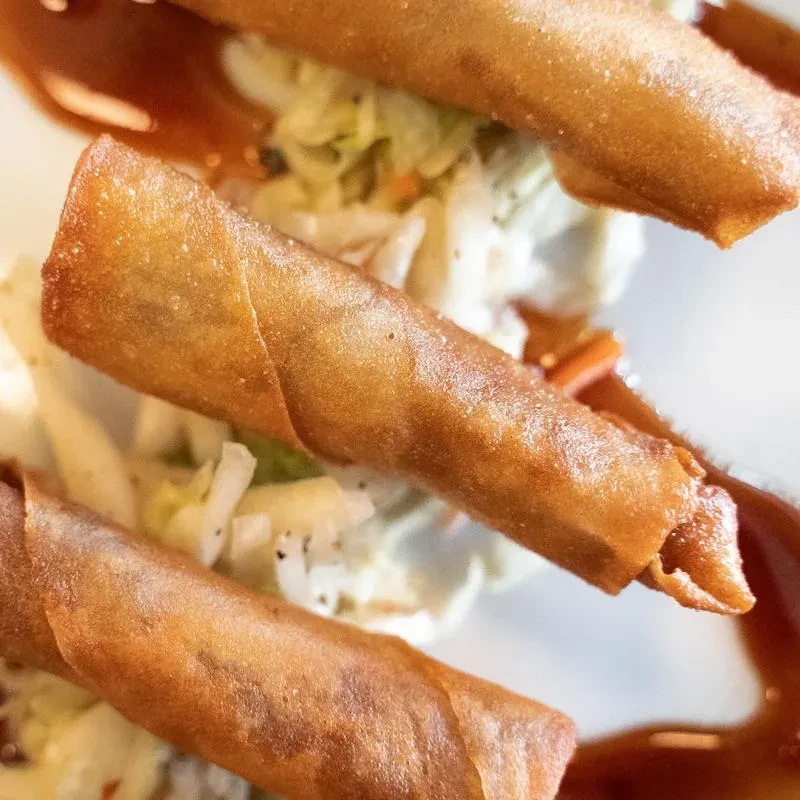 Three golden-brown fried spring rolls on lettuce with sauce.