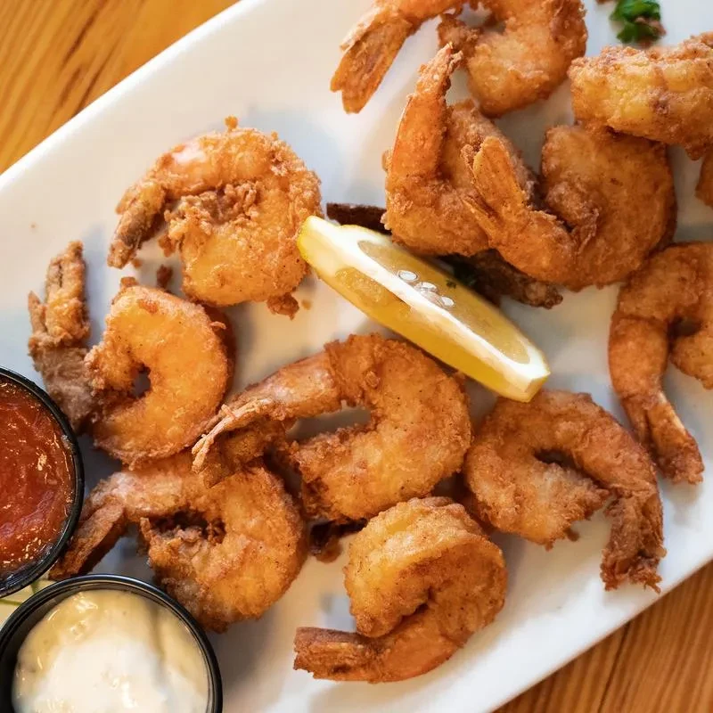 Golden fried shrimp, lemon, and two dipping sauces on a white plate.