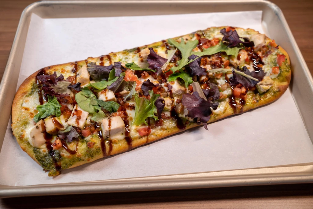 Pesto flatbread pizza with chicken, cheese, tomatoes, lettuce, and balsamic glaze.