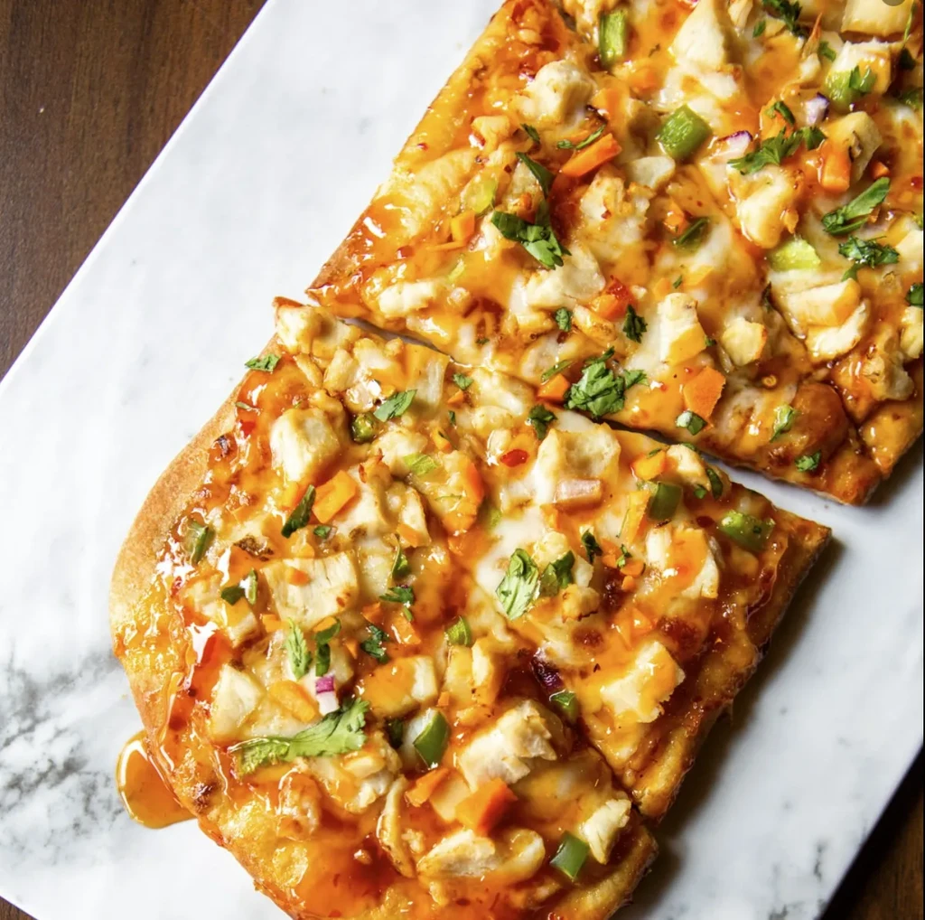 Rectangular chicken flatbread with vegetables, herbs, and amber sauce.