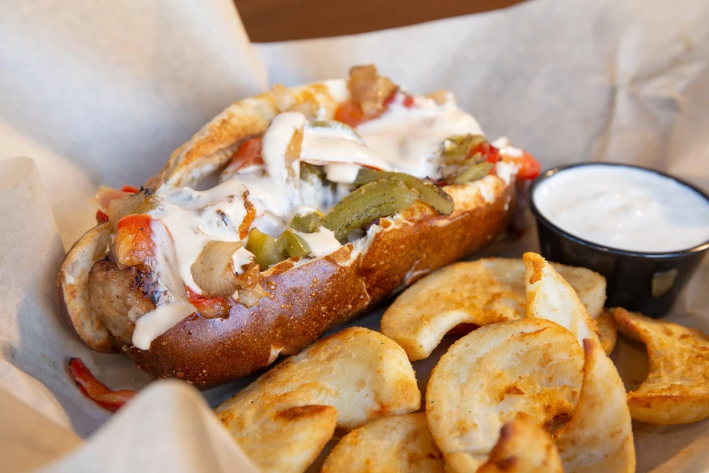 Sausage sandwich with peppers, onions, fries, and two creamy sauces.