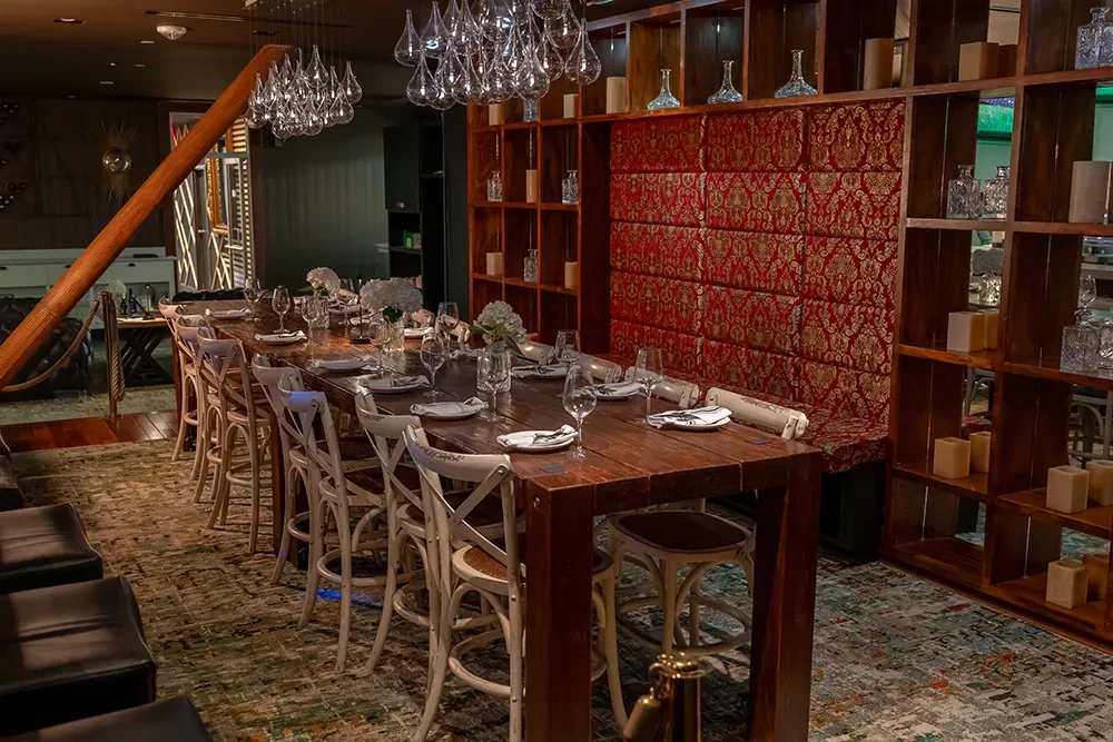 Sophisticated dining room: rustic communal table, red banquette, unique chandeliers.