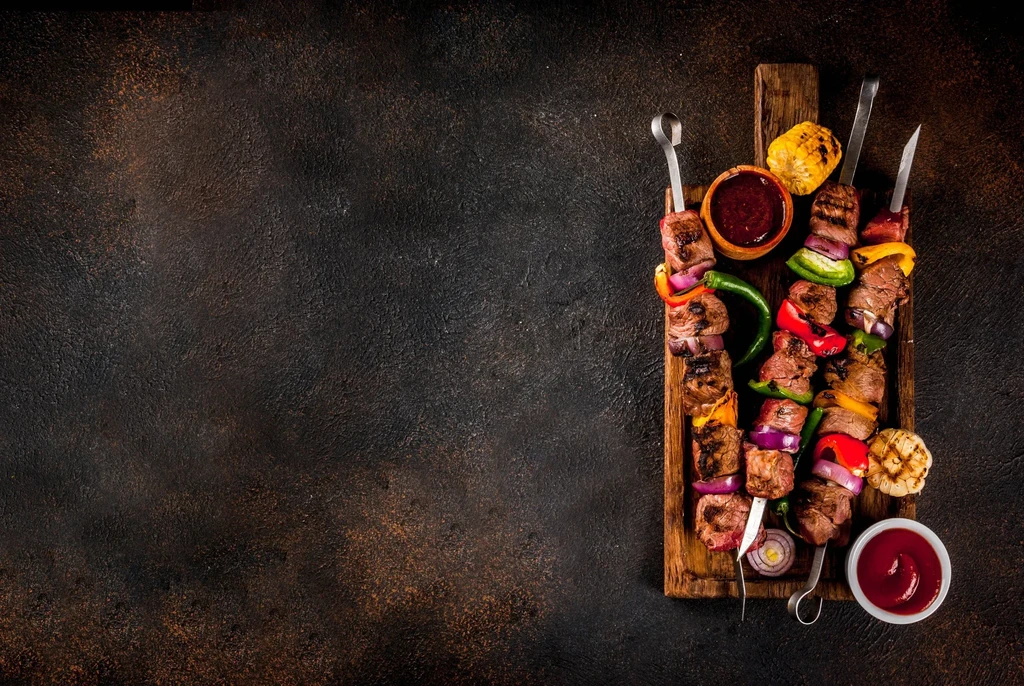 Three grilled meat and vegetable skewers with corn, garlic, and sauces.