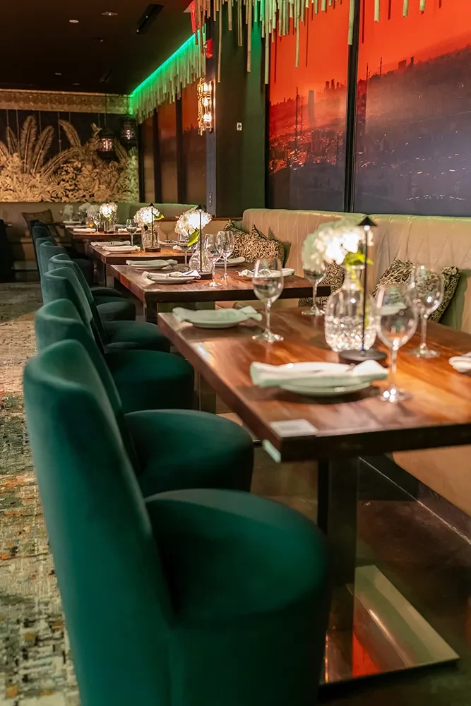 Restaurant interior with teal chairs, two murals, and green LED lighting.