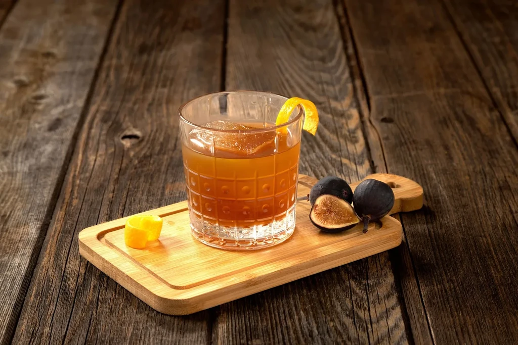 Amber cocktail in textured glass with figs and orange peel.