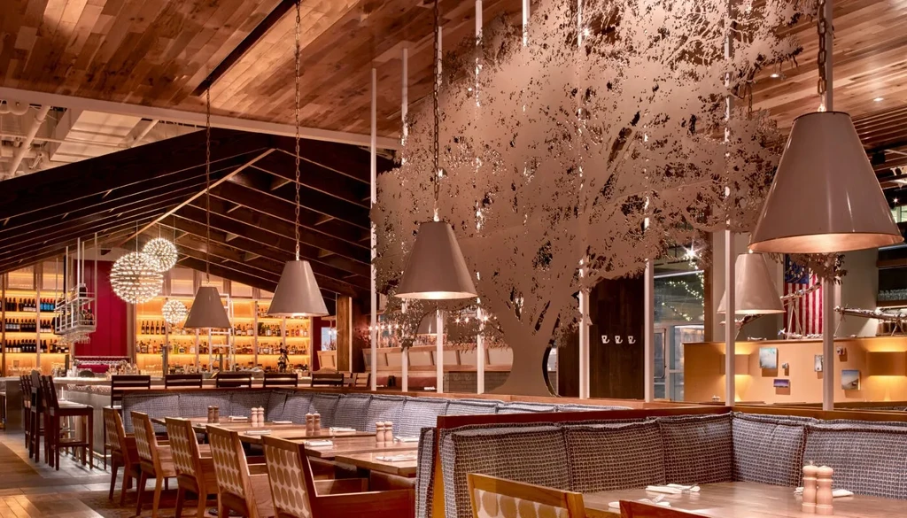 Restaurant interior with wooden vaulted ceiling, tree screen, and stocked bar.