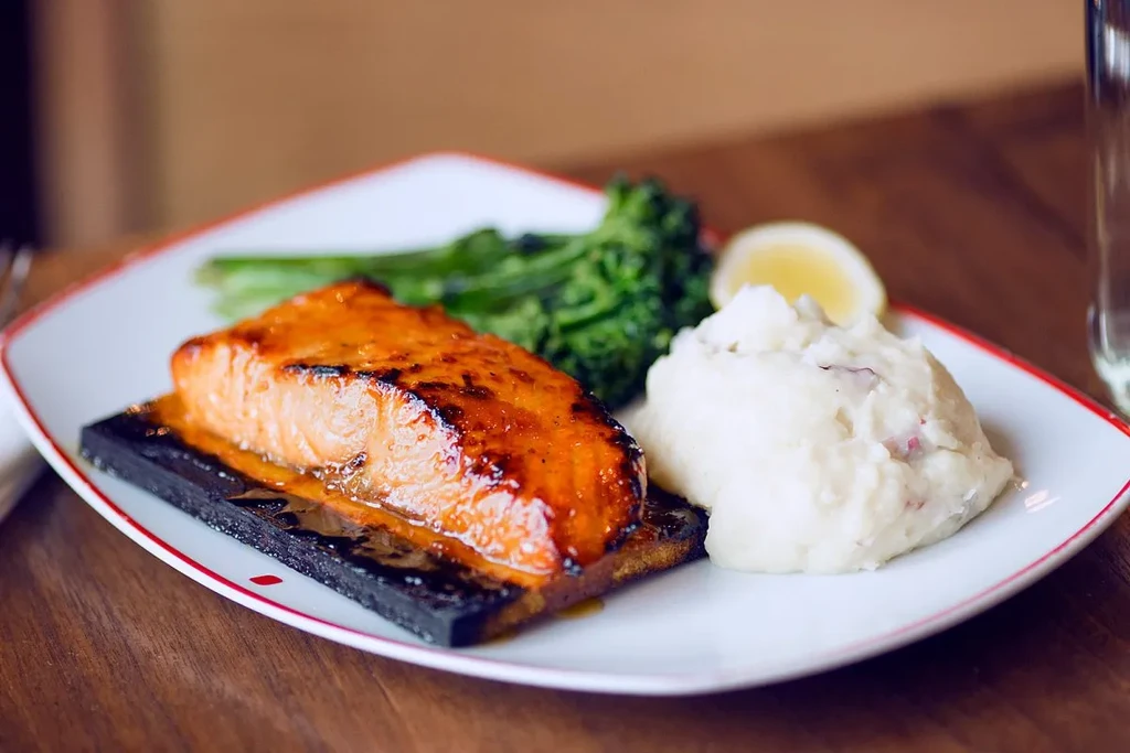 Glazed salmon on a plank with broccoli and red skin mashed potatoes.
