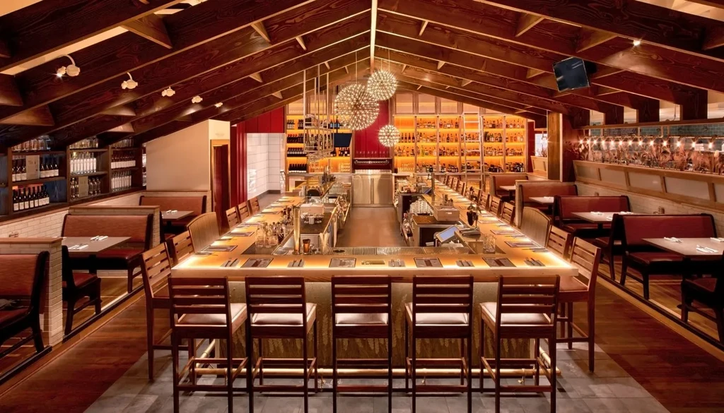 Modern, empty restaurant with a U-shaped bar, liquor shelves, and chandeliers.